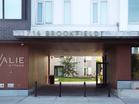 Ottawa, Ontario, Canada &ndash; July 26, 2025: The "716 Brookfield" entrance features a modern breezeway with wood paneling, black bollards, and "The Revalie" signage on the exterior.