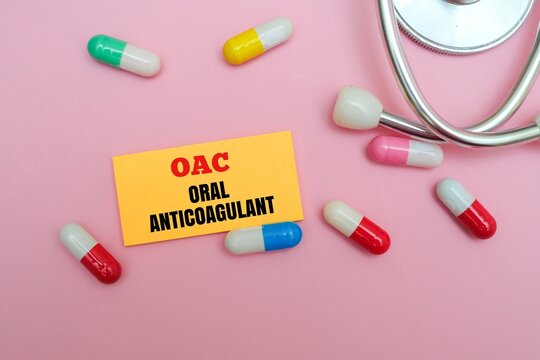 A yellow note with the text OAC - ORAL ANTICOAGULANT surrounded by various multi colored medicinal capsules and a stethoscope. Related to heart health, blood thinners and cardiovascular treatment