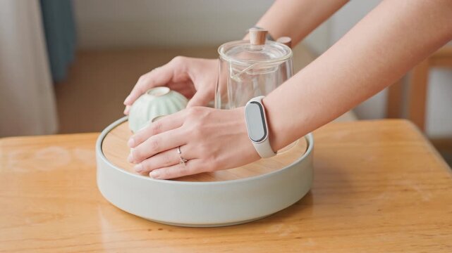 Hotel room tray with two bowls and glass, hands pick up bowls and carry tray away from table, crumbs on tray base, soft daylight and cozy interior emphasize casual hospitality cleanup