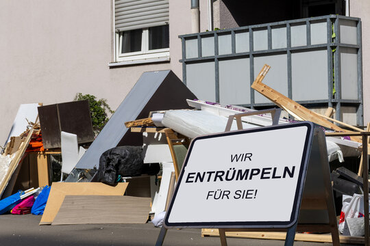 Hausrat vor einem Wohnhaus, davor ein Schild mit der Aufschrift WIR ENTR&Uuml;MPELN F&Uuml;R SIE