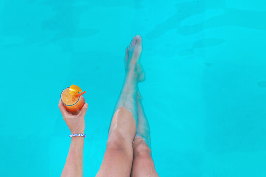 Cocktail in hands of woman against the background of swimming pool. Selective focus.