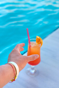 Cocktail in hands of woman against the background of swimming pool. Selective focus.