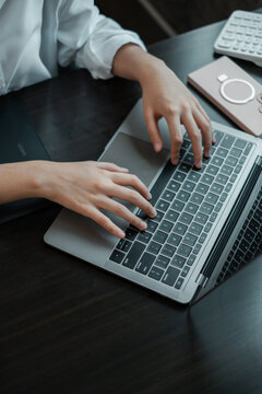 Close-up of hands typing on a laptop keyboard, surrounded by tech gadgets on a wooden desk in an office environment.