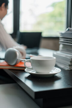 A serene office setting featuring a coffee cup, headphones, and stacked documents on a desk by a window.