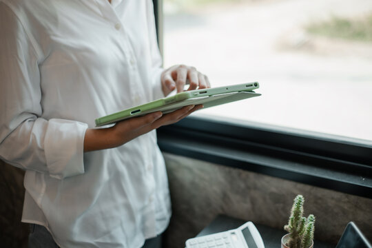A business professional interacts with a tablet by a window, showcasing modern technology in a minimalist office environment.