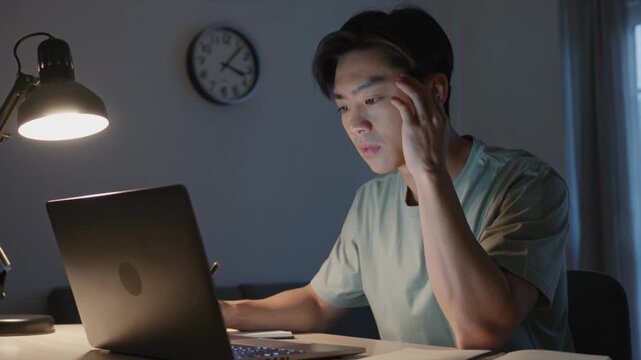 Dedicated man working alone late at night at his desk illuminated by a single desk lamp in an otherwise completely dark office