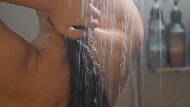 Hotel shower hair rinse under warm stream, traveler with visible ring massaging nape and scalp, subtle bathroom shelf with toiletries in background, closeup of hands and wet strands conveying endofday