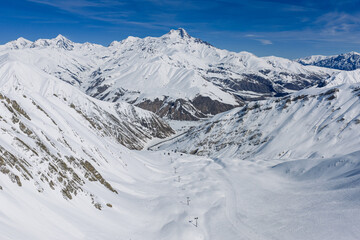Fototapeta premium Aerial view of Mount Kazbek sunny winter day with snow covered mountains and clear sky, Kazbegi region near Gudauri, Georgia. Mount Kazbek bright sunlight and clear sky in Caucasus Mountains, Georgia