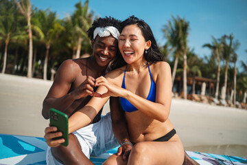 Fototapeta premium Trendy digital creator couple taking selfie by the beach, sharing travel content for social media