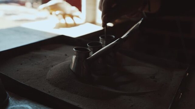 Traditional process of making Turkish coffee in a copper cezve on hot sand. Close-up of brewing coffee with foam rising, authentic oriental preparation method