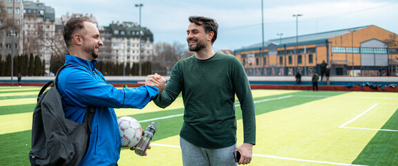 Two men shake hands on a soccer field after a game in the afternoon with clouds in the sky © Marko