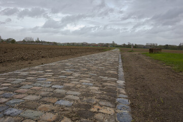 Fototapeta premium route réfectionner en pavé emprunté par la course cycliste du paris Roubaix secteur Templeuve avec un ciel gris menaçant