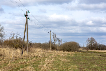 Fototapeta premium Power line poles in rural field under cloudy sky