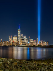 Naklejka premium New York City night view of Lower Manhattan skyline with memorial Tribute in Light spotlight beams and reflections on the Hudson River