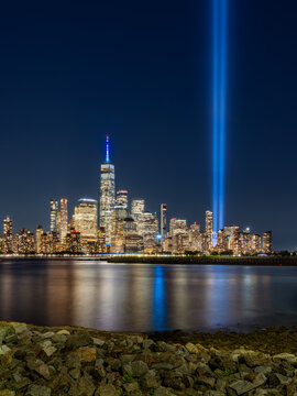 New York City night view of Lower Manhattan skyline with memorial Tribute in Light spotlight beams and reflections on the Hudson River