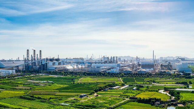 Extensive industrial park and chemical manufacturing facilities located next to vibrant green agricultural fields under a clear blue sky.
