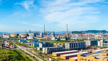Obraz premium Modern industrial zone with large storage silos and factory buildings near the harbor under blue sky.
