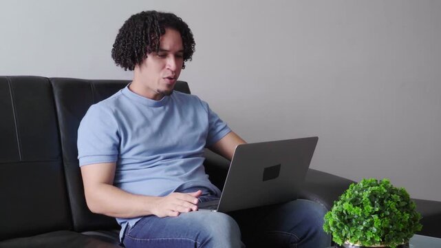 Hispanic man sits on a couch while using his laptop for a telemedicine appointment with a doctor