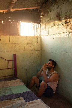 A criminal is crying, showing remorse and frustration, while sitting next to a bed in his cell inside a prison in Neiva, Huila, Colombia. Concept of sadness and psychological trauma