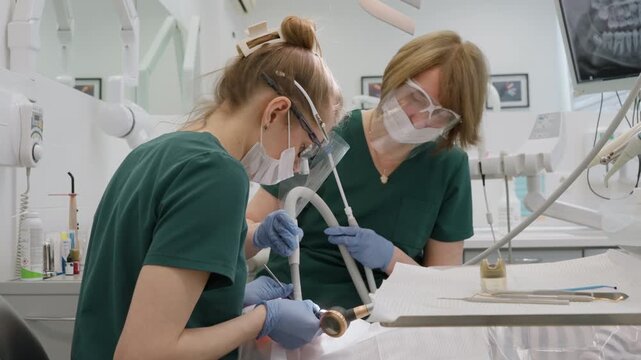 Professional dentist using air flow sandblasting for plaque removal while assistant holding suction tool. Teamwork in stomatology clinic for patient oral hygiene care and prophylaxis service