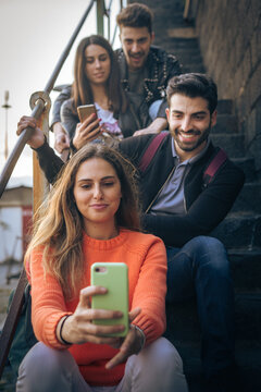 Group of Friends Taking a Selfie on Staircase Using Smartphones, Emphasizing Social Connection