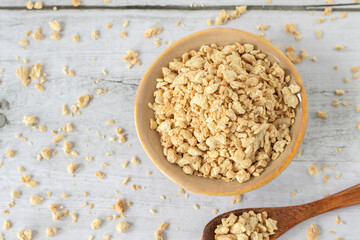 Bowl of textured (dehydrated) soy protein granules on wooden background. Top view.