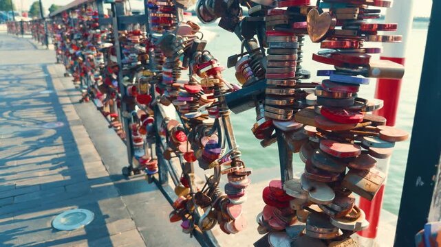 Colorful love padlocks symbolizing everlasting romance and commitment secured to a bridge railing along a river on a bright sunny day, representing travel tradition and relationships