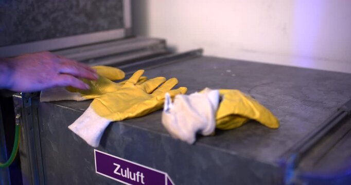 Close up of worker hands putting yellow protective safety gloves on a metal workbench in a workshop