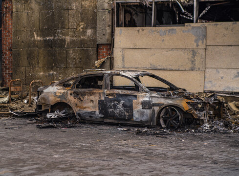 Burned out car wreck abandoned on city street. Destroyed vehicle after fire accident. Vehicle hulk as result of war conflict or arson. Urban catastrophe and property damage concept.