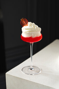 Red cocktail with creamy foam and strawberry garnish served in elegant glass on minimal background