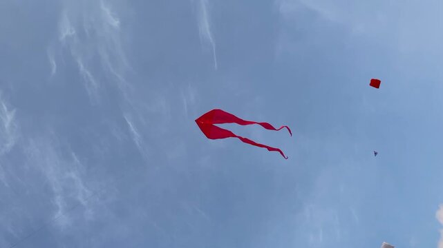 Bright kites soaring in a clear blue sky, capturing a playful outdoor moment with light clouds and wind