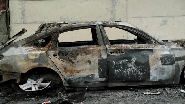Burned out car wreck abandoned on city street. Destroyed vehicle after fire accident. Vehicle hulk as result of war conflict or arson. Urban catastrophe and property damage concept.