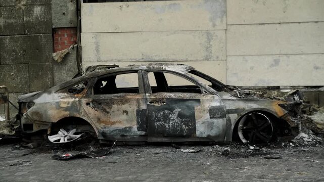 Burned out car wreck abandoned on city street. Destroyed vehicle after fire accident. Vehicle hulk as result of war conflict or arson. Urban catastrophe and property damage concept.