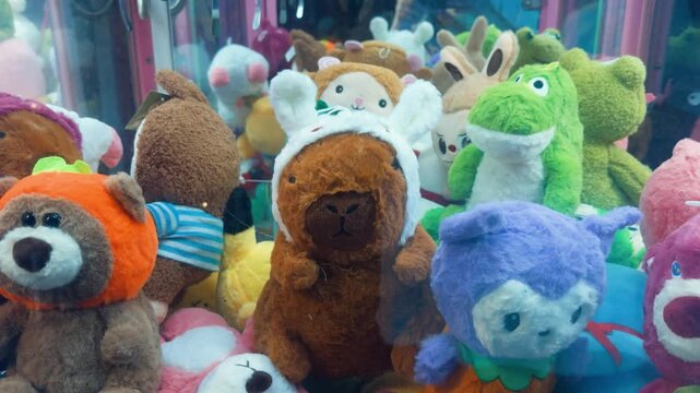Capybara plush wearing bunny ears perched in a colorful arcade claw machine pile, evoking childhood excitement, playful prizes, and the hope of winning a beloved stuffed toy