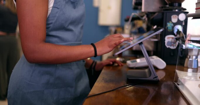Close up of a female barista wearing a blue apron taking an order on a modern touchscreen point of sale system at the counter of a cozy coffee shop, with pastries visible nearby