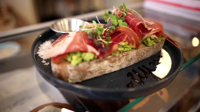 Freshly prepared gourmet bruschetta with avocado spread and cured prosciutto ham, garnished with microgreens and balsamic glaze, served on a stylish plate in a restaurant setting
