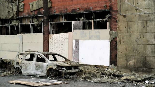 Burned out car wreck abandoned on city street. Destroyed vehicle after fire accident. Vehicle hulk as result of war conflict or arson. Urban catastrophe and property damage concept.