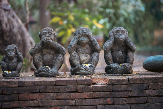 Three wise monkeys stone statues in garden with symbolic meaning, See hear speak no evil sculpture set with traditional Asian philosophy concept