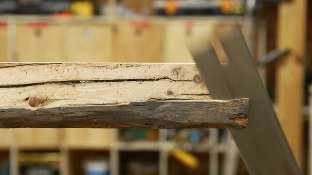 Carpenter cutting a wooden plank with a handsaw in a workshop
