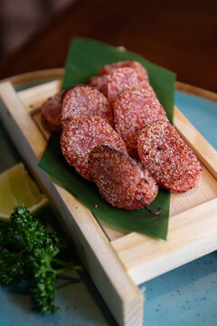 Pink sesame crusted grilled mentaiko slices on banana leaf with lime wedge and parsley garnish, warm appealing food presentation