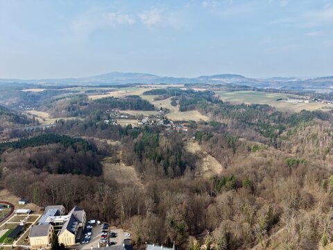 Forest hills meet city outskirts. Aerial perspective captures suburbs beside wooded mountain slope