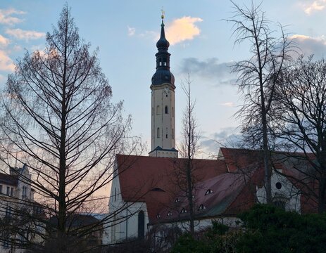 Ancient church tower with bare trees and pastel sunset illuminating tranquil village scene
