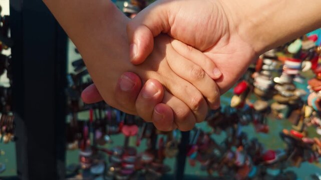 Couple's hands intertwined, representing romantic love, strong partnership, togetherness, and lasting commitment, with blurred background of numerous love padlocks signifying eternal bonds