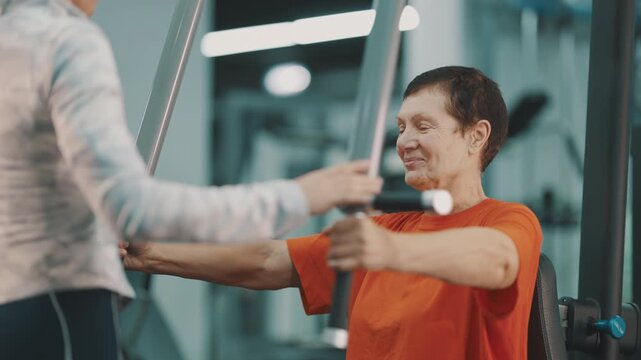 Senior woman training on a chest press machine with a coach