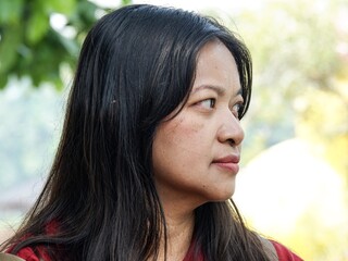 Side profile portrait of a mature Asian woman with long black hair looking away thoughtfully. A natural headshot captured outdoors in soft daylight, reflecting a calm and serene expression. © agung