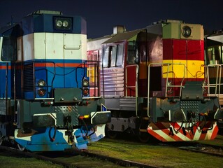 Contrasting locomotives parked at night. Silent engines with chevron bumpers under moody depot lighting © Vladimir