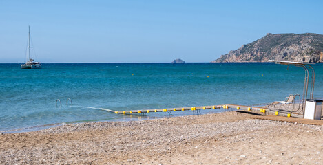 Fototapeta premium Accessible beach pathway with floating platform and handrails extending into blue sea, Chios island, Greece
