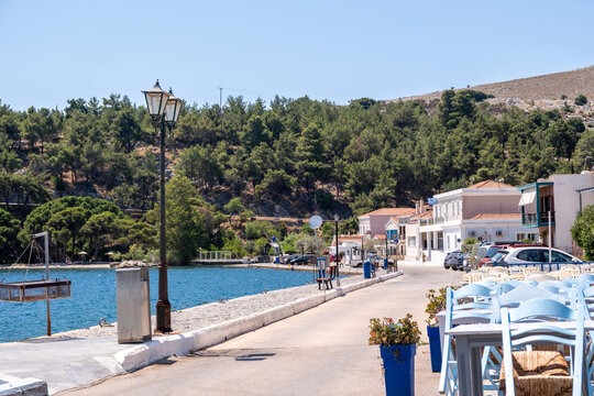 Sunny seaside promenade with traditional houses and blue chairs in Chios island Greece