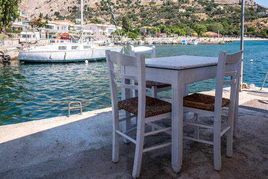 Seaside taverna table and chairs, sailboats in a sunny harbor Chios island Greece