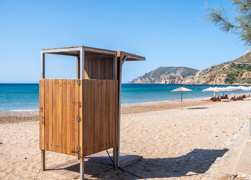 Wooden outdoor change room and shower on Komi sandy beach, Chios island, Greece. Sun umbrellas and sunbeds, summer day.
